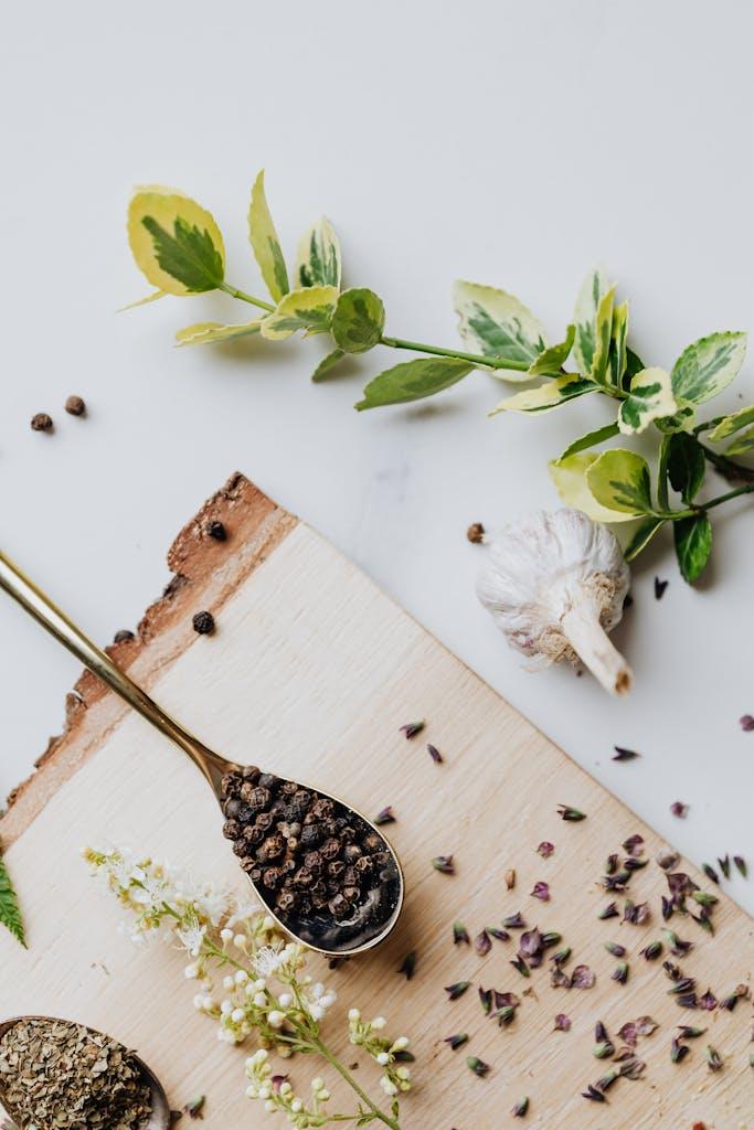 A top-down view of garlic, peppercorns, and herbs on a wooden board with a fresh, natural vibe.