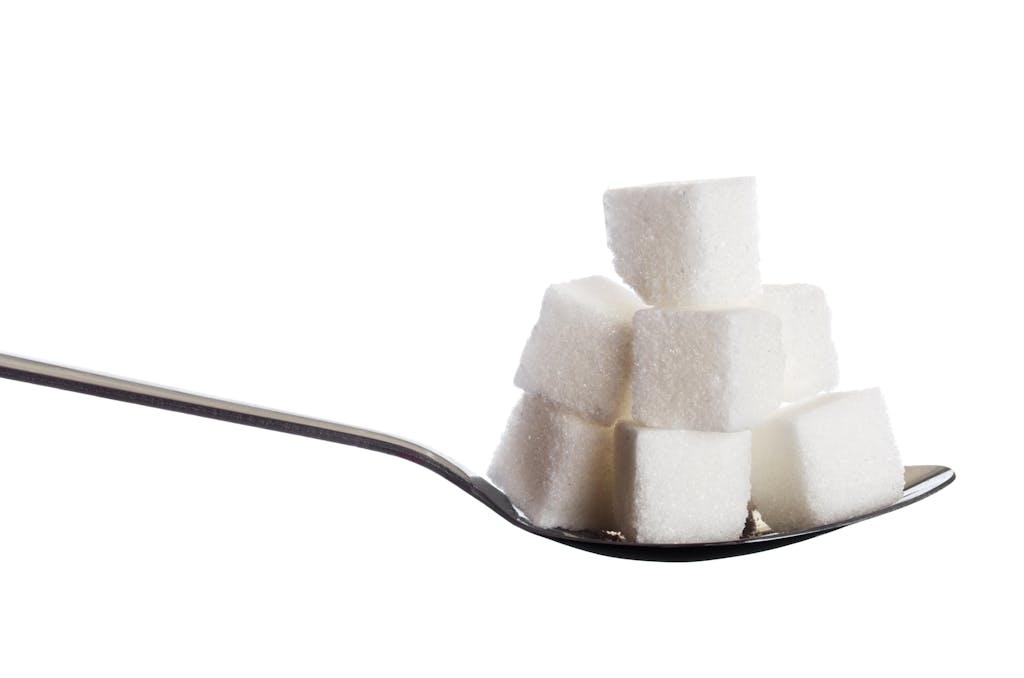 Close-up of sugar cubes stacked on a spoon against a white background, highlighting simplicity and sweetness.