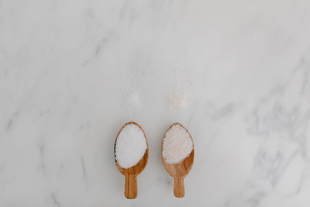 Minimalist still life of two wooden spoons with salt on a marble background.